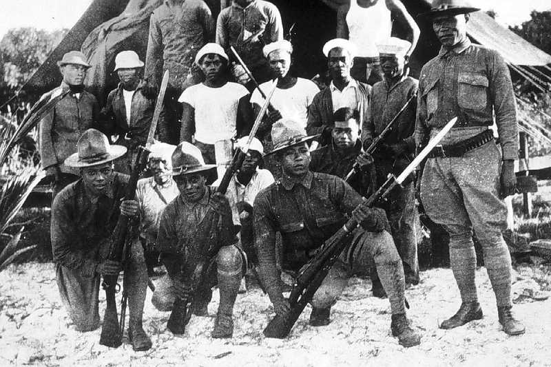 Filipino constabulary in uniform pose with rifles in front of civilians