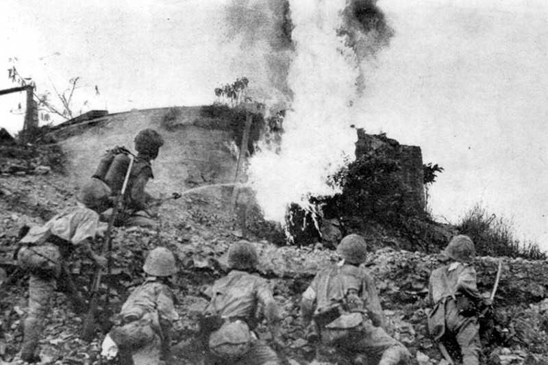 Photo of soldiers standing behind barrier, one shooting flames above them