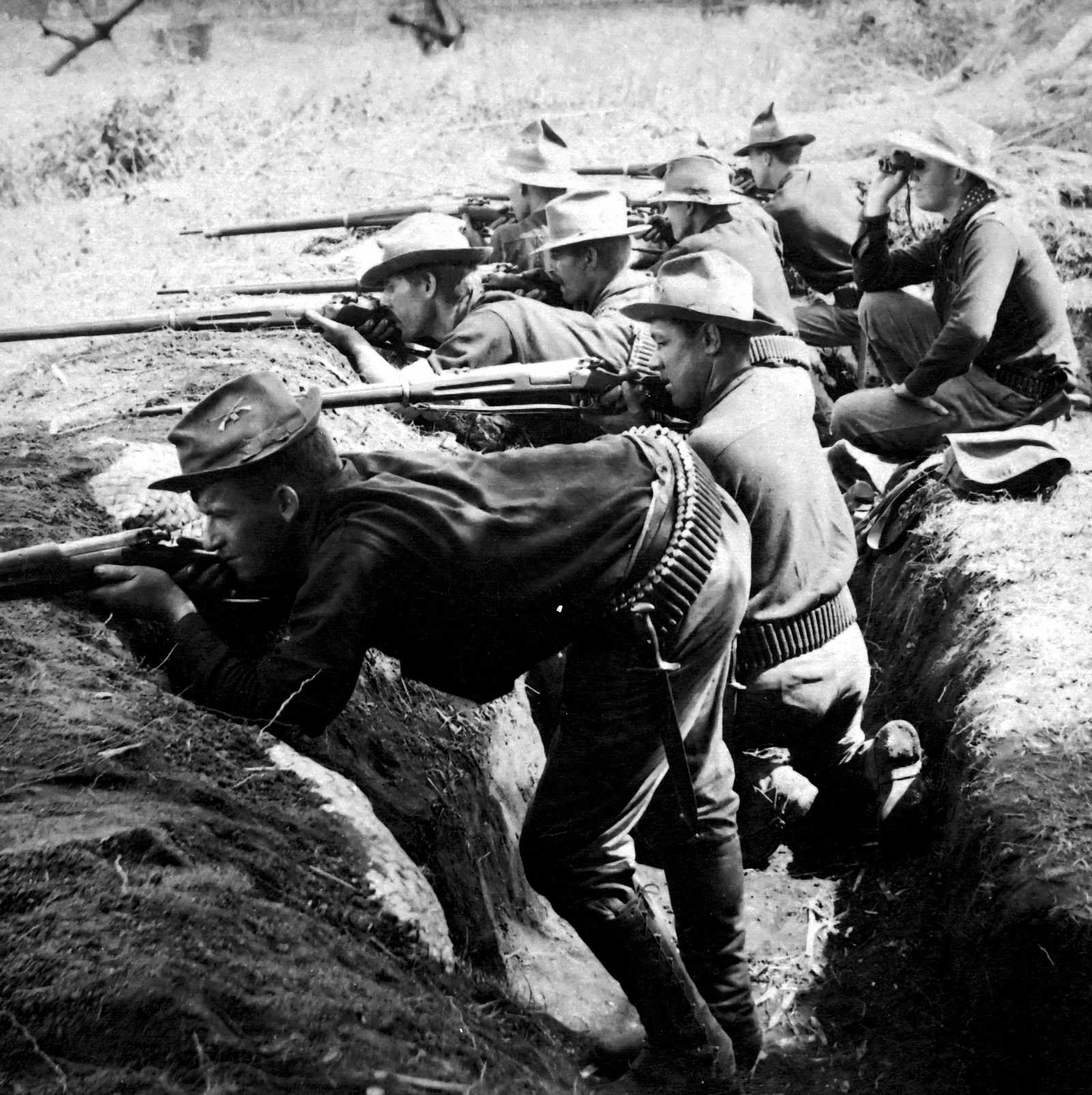 Black and white photo of soldiers aiming their rifles out of a trench