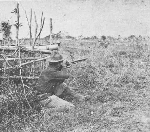 Black and white photo of crouching soldier aiming rifle into field