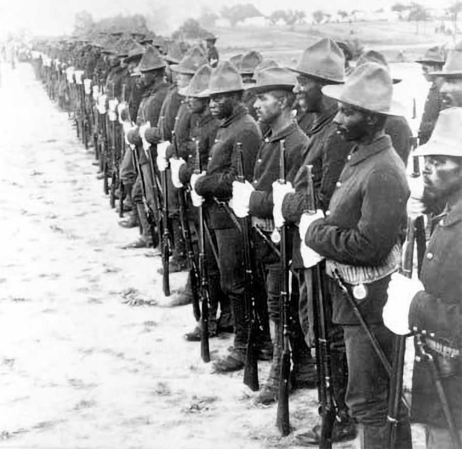 Black and white photo of African American soldiers lined up in uniform and holding their rifles